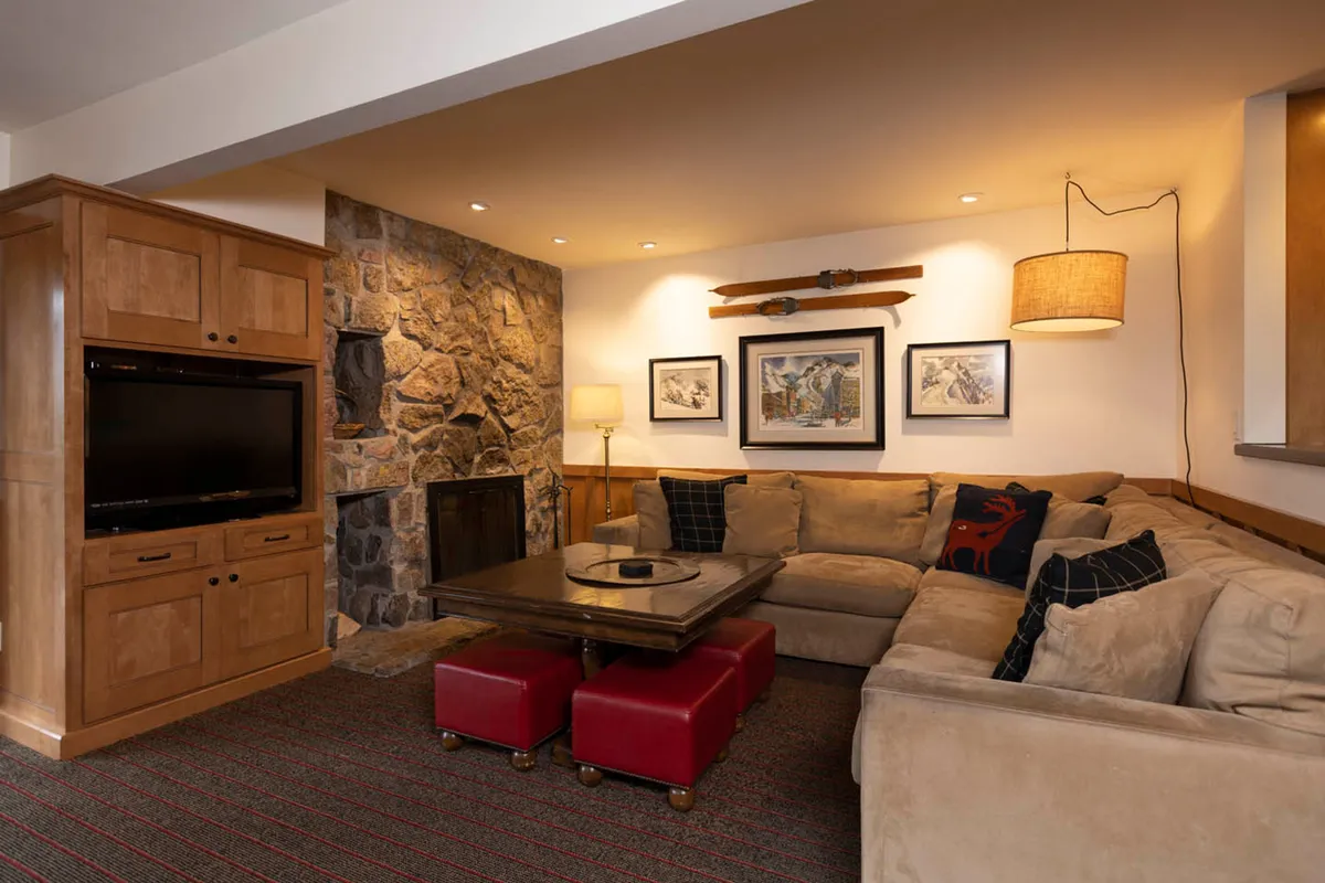 A spacious living room featuring a large sectional sofa arranged around a substantial stone fireplace, with a coffee table at the center and tasteful artwork adorning the walls. The room exudes warmth and comfort, inviting guests to gather, converse, and unwind after a day on the slopes.