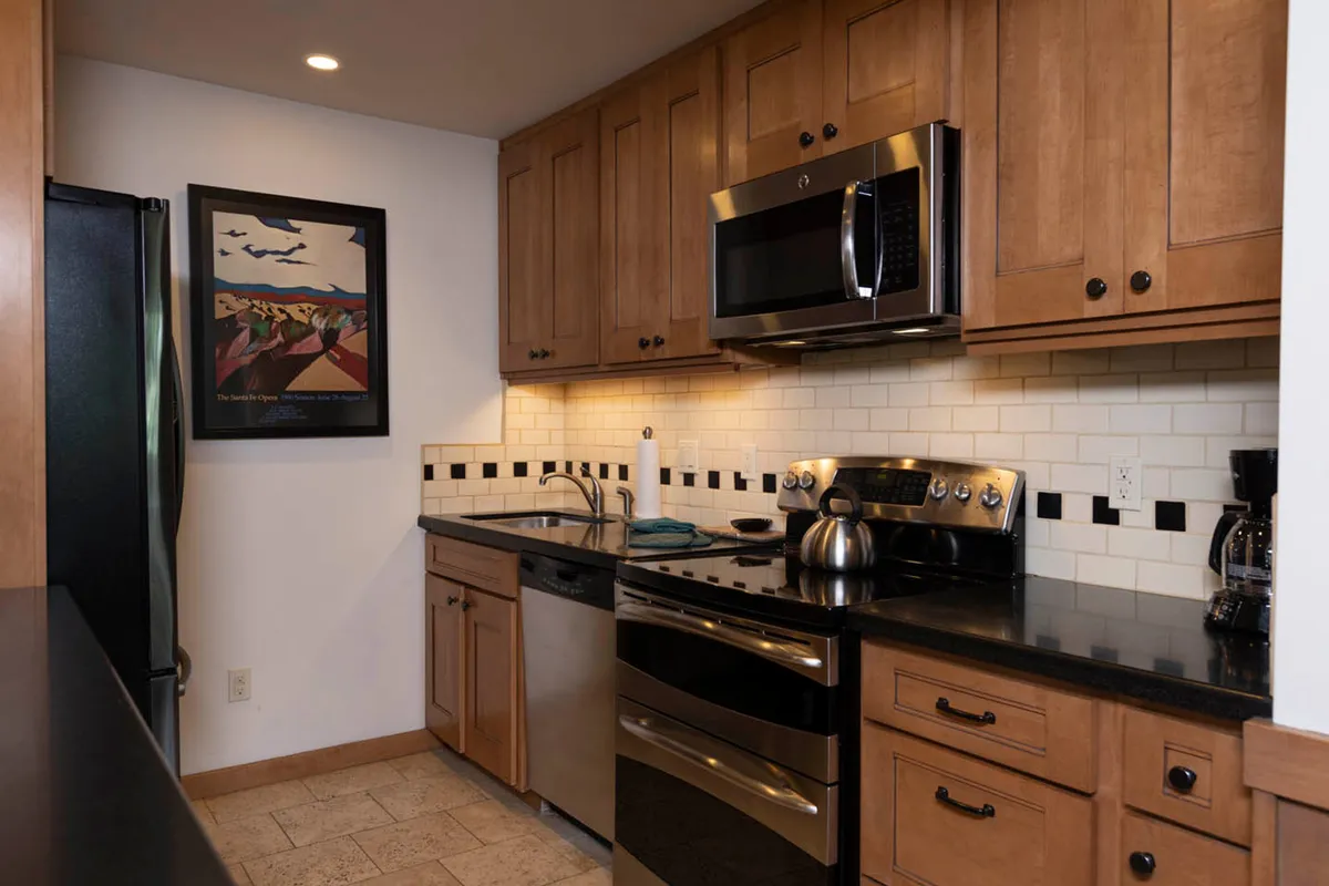 A well-appointed kitchen with stainless steel appliances, a black countertop, wooden cabinetry, and a white tiled backsplash with black accents. The space is practical yet inviting, providing an ideal setting for preparing group meals or sharing snacks after a day outdoors.